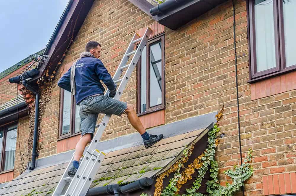Guttering contractor from 1Call Roofing team climbs ladder to work on guttering system on residential property in Dorset